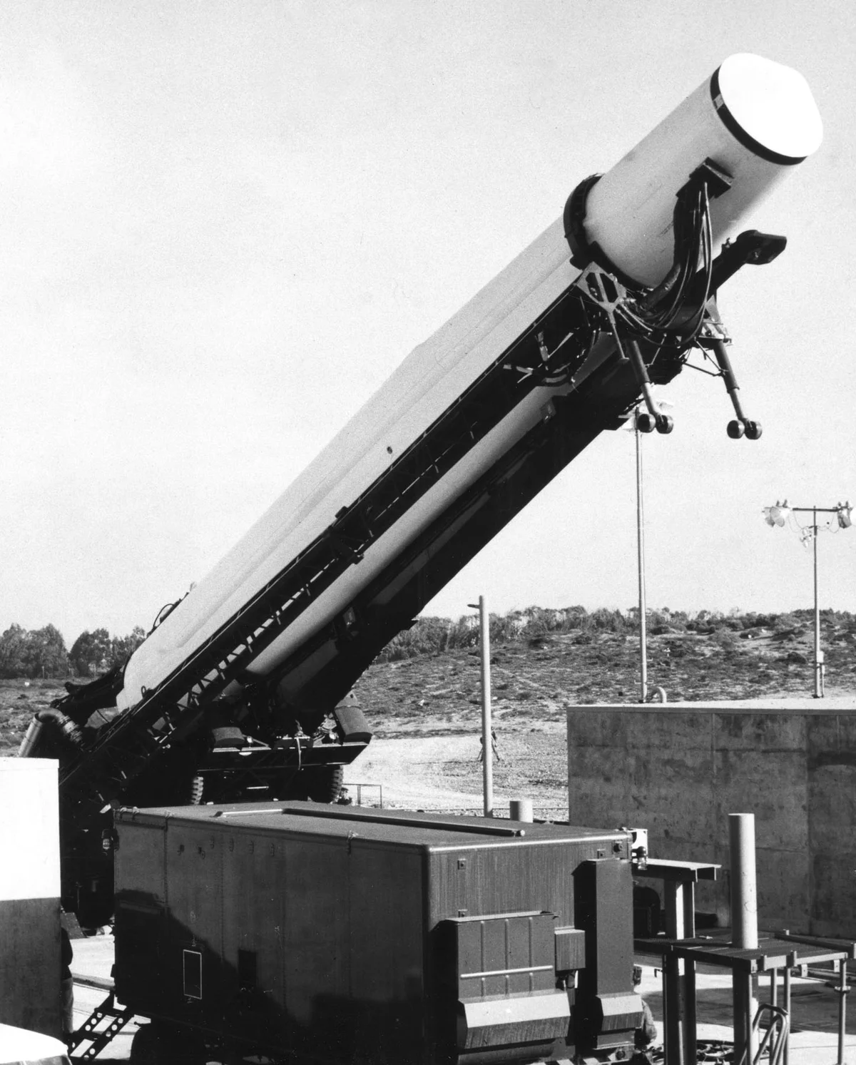 A Thor missile being raised on its erector, above a concrete emplacement and associated equipment.